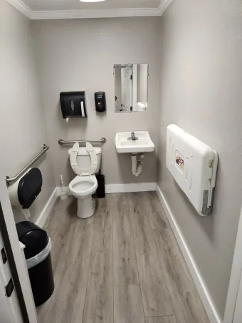 Small accessible restroom with toilet, sink, grab bars, mirror, and trash bins in a gray room | Dillsboro Automotive