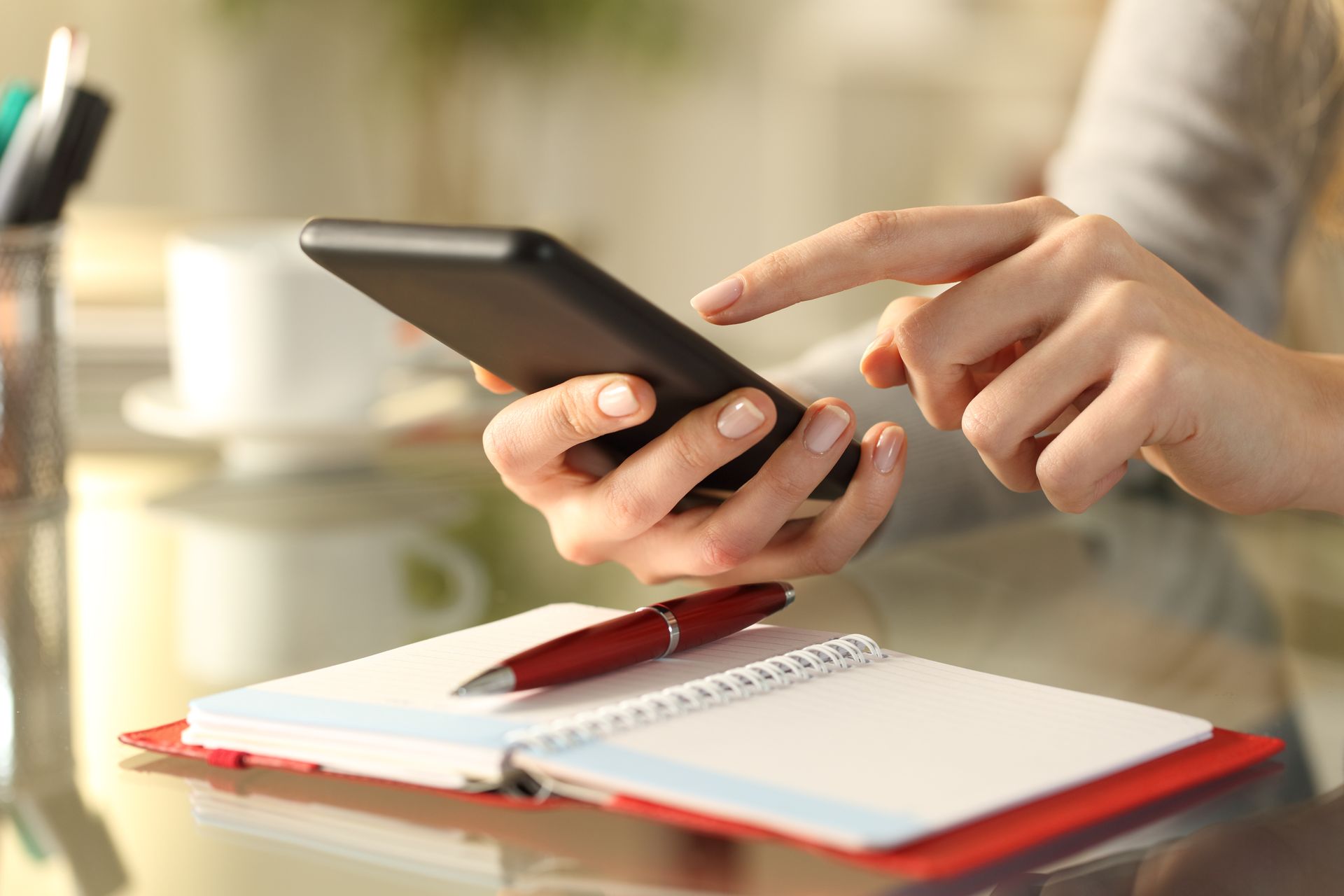 Person holding a smartphone showing a colorful calendar app at a desk with a keyboard and monitor | Dillsboro Automotive