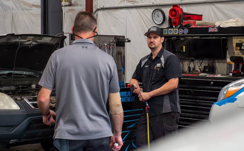 Two men talking in a garage workshop near a black car and tool cabinets | Dillsboro Automotive