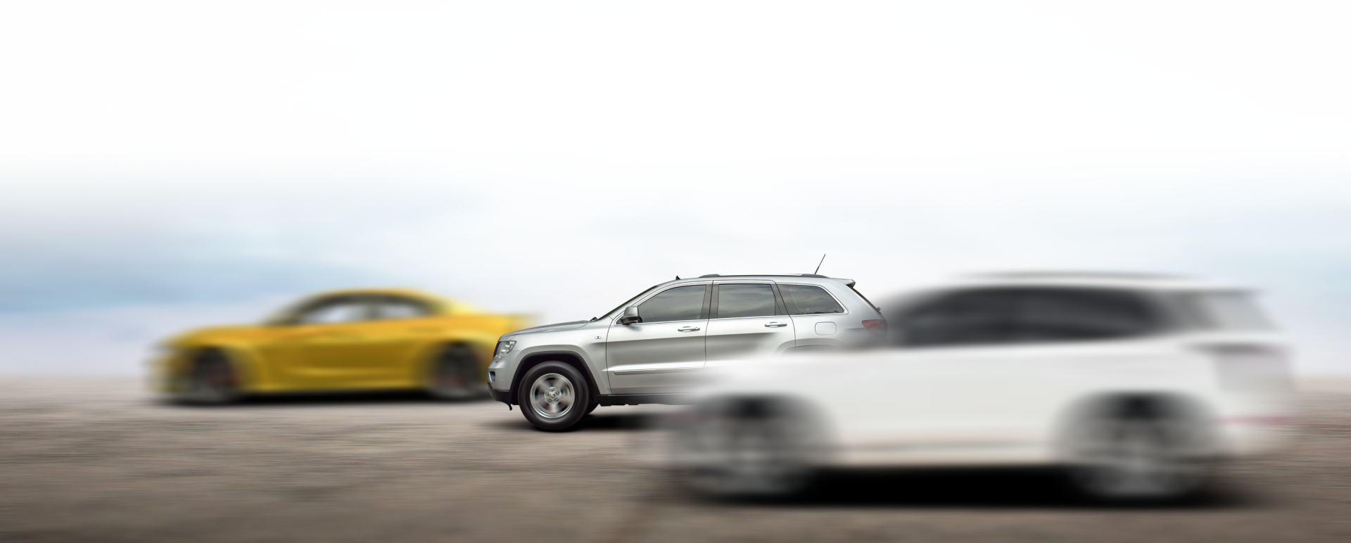 Three cars speeding across a blurred landscape, with a yellow coupe, silver SUV, and white hatchback. | Dillsboro Automotive