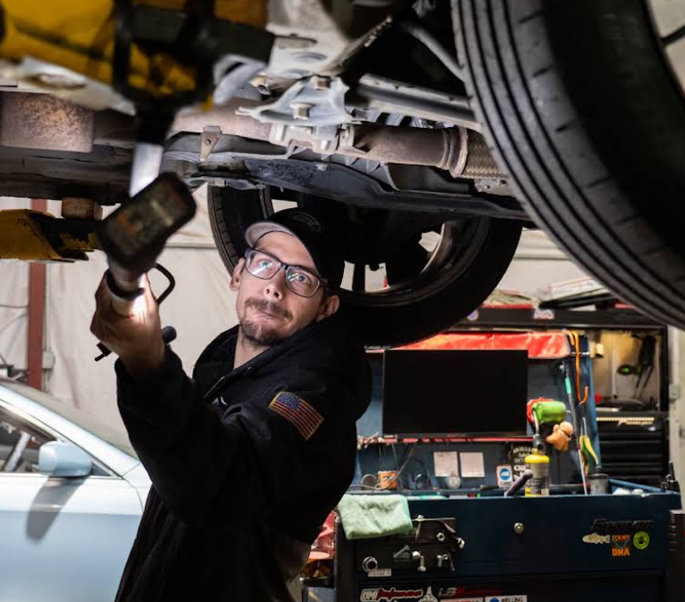 Mechanic working under a car on a lift, using a tool in an auto repair shop. | Dillsboro Automotive