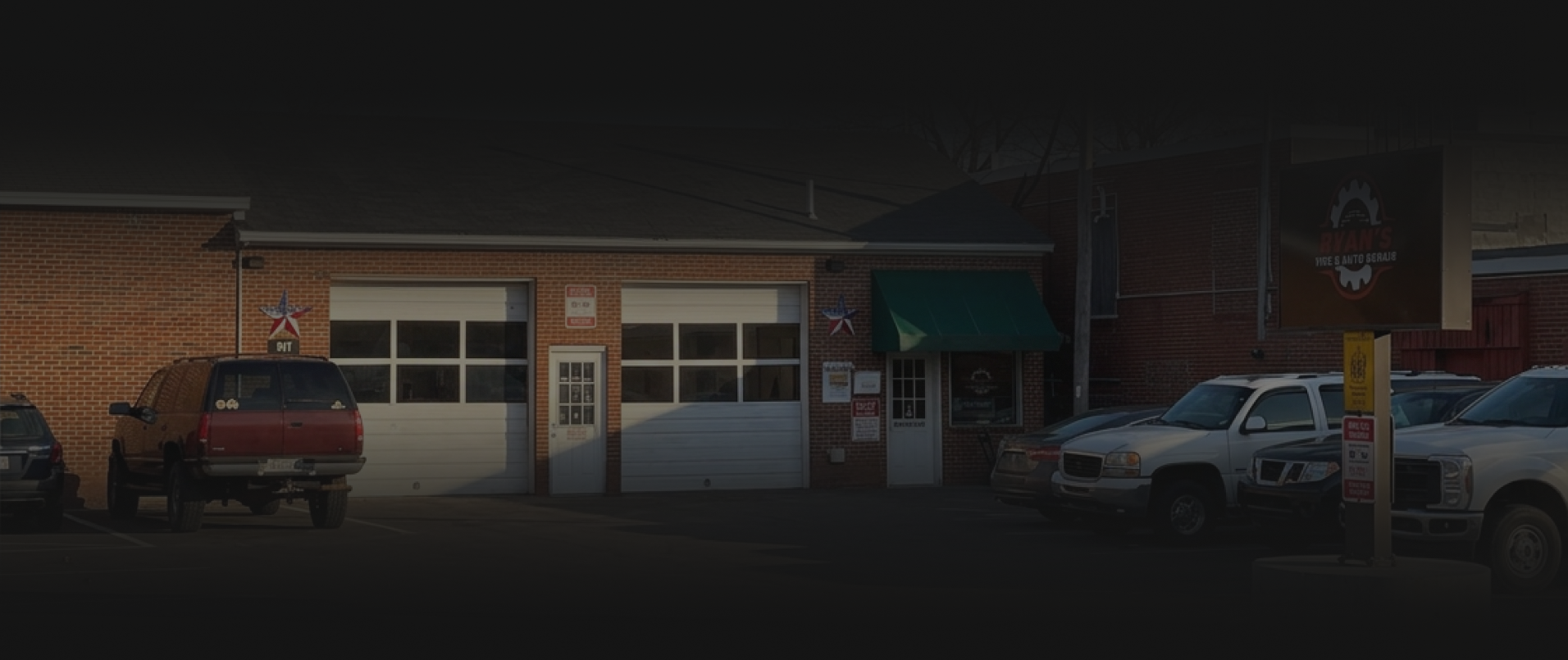 Brick storefront with two garage doors, parked red SUV on the left and white pickup on the right. | RyansTireAutoRepair