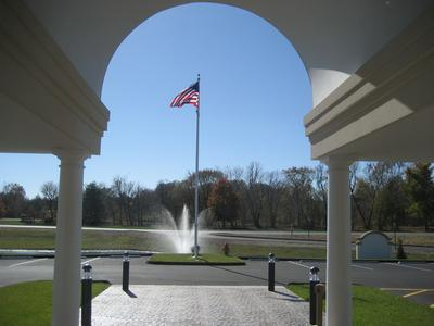American flag flying over a fountain in a park, framed by a white archway