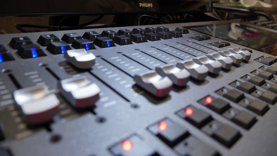 Close-up of a studio mixing console with sliders, knobs, and glowing indicator lights