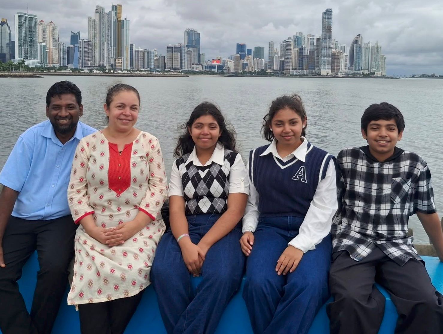 Five people sitting by the water with a city skyline in the background.