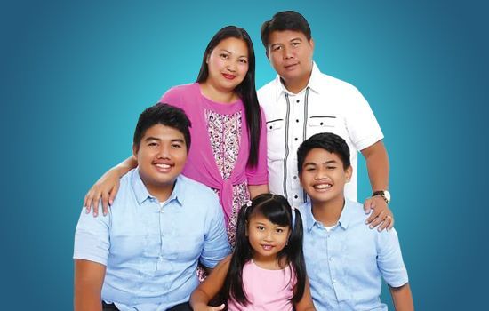 Five people posing together against a blue studio backdrop, smiling and standing close.