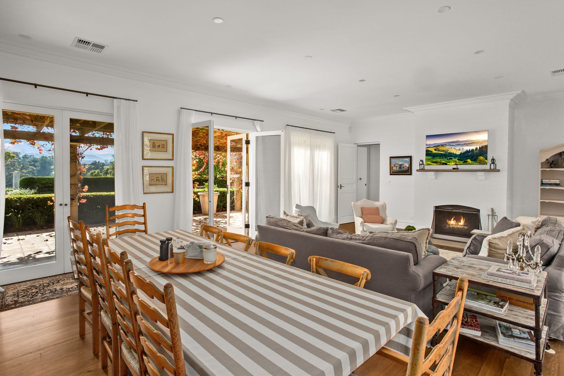 Bright Dining And Living Room With Striped Tablecloth, Gray Sofas, And A Lit Fireplace — Shona Design In Mittagong, NSW