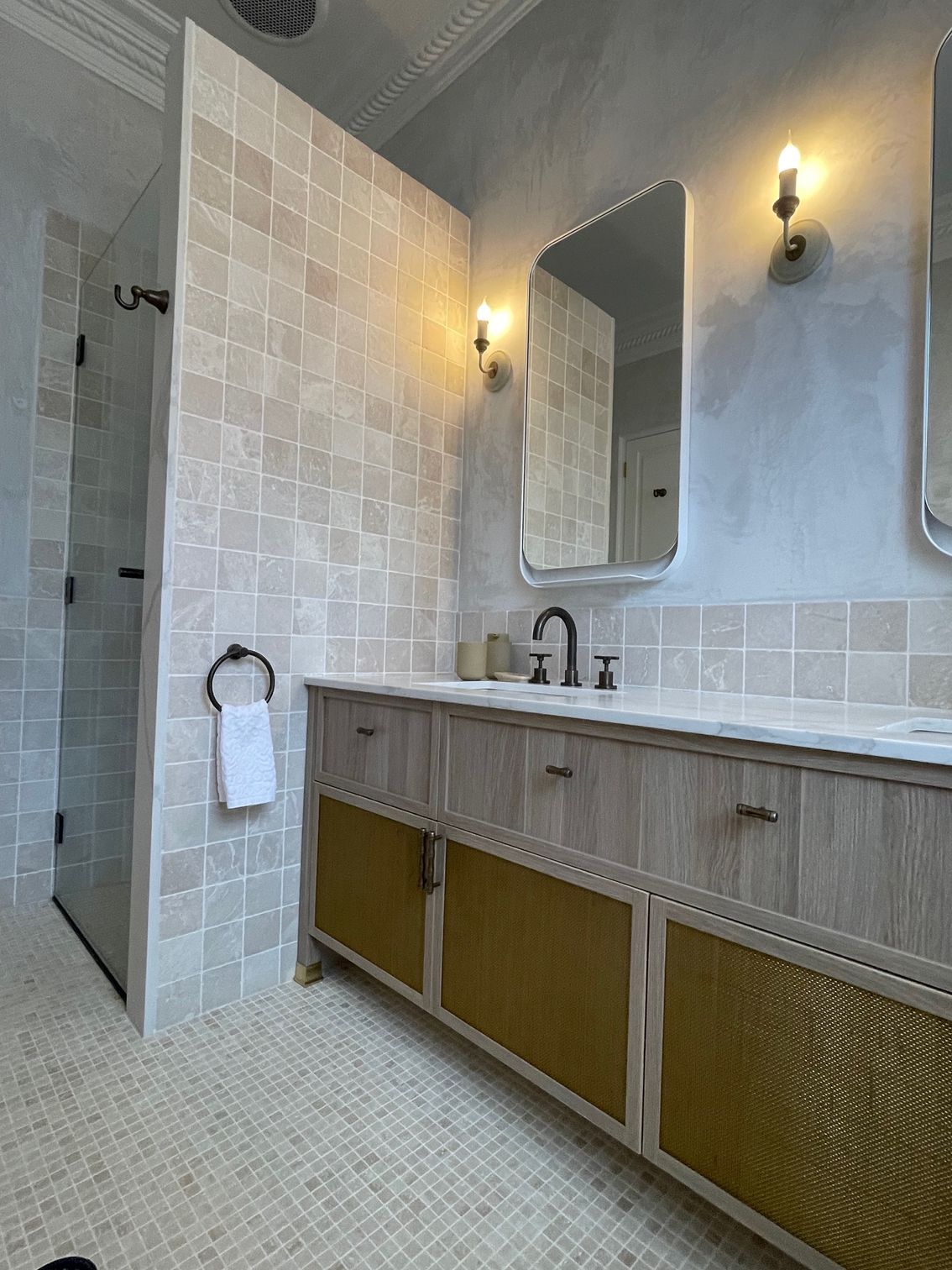 Modern bathroom with light tile, wood vanity, mirror, and wall sconces 