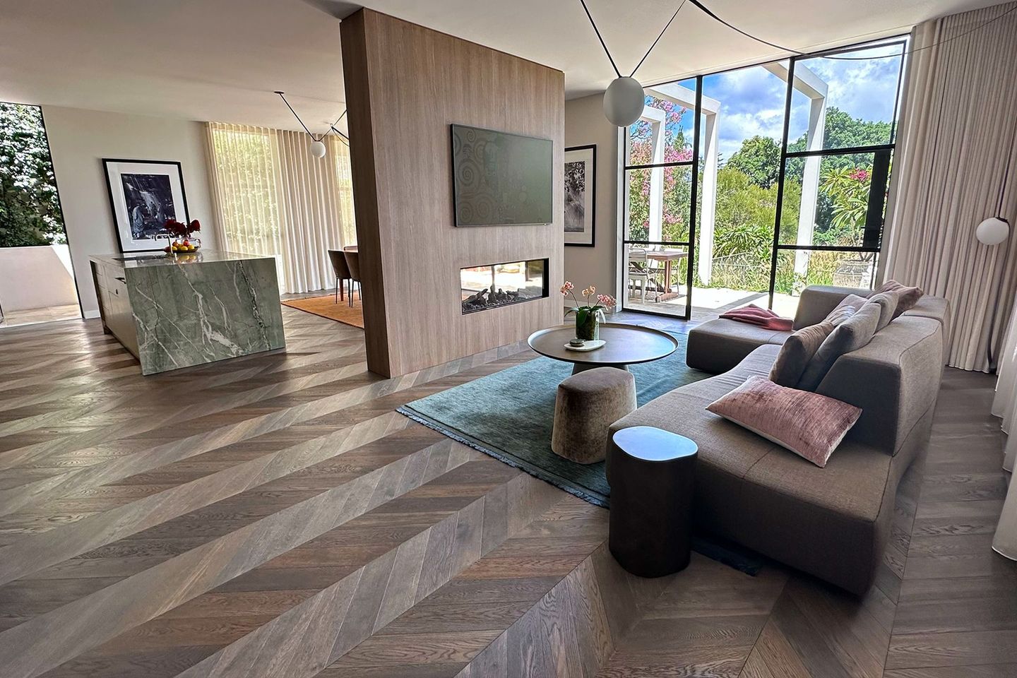 Modern living room with gray sectional, wood floors, marble fireplace, and large windows overlooking greenery — Shona O'Brien Interior Design in Bowral, NSW