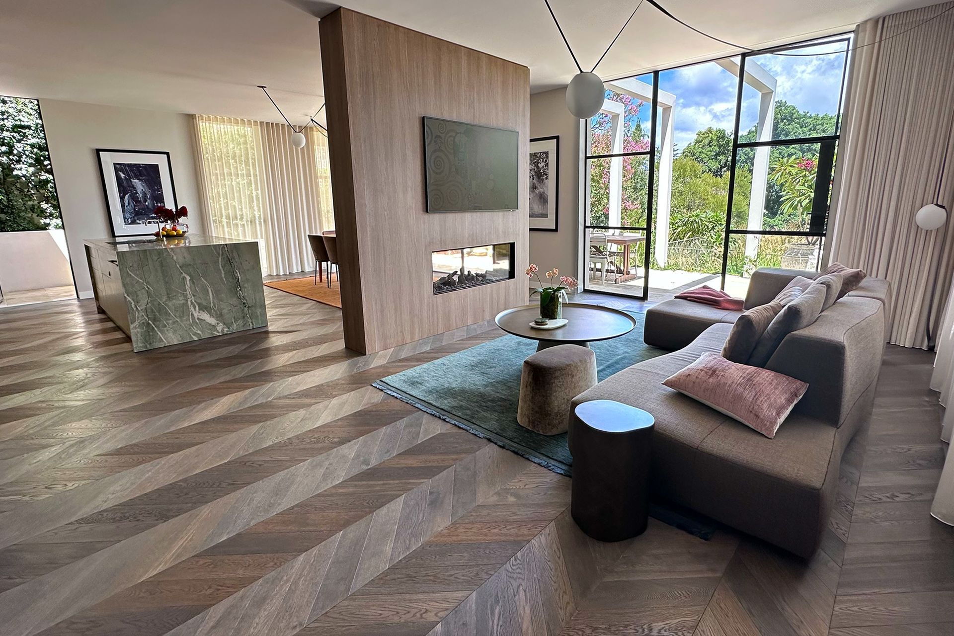 Modern living room with gray sectional, wood floors, and large windows overlooking greenery — Shona O'Brien Interior Design in Bowral, NSW