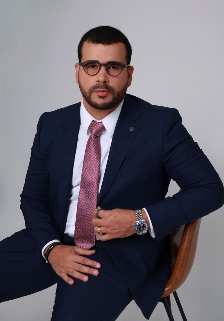 Jorge Henrique Silva De Melo. A man in a suit sitting on a chair.