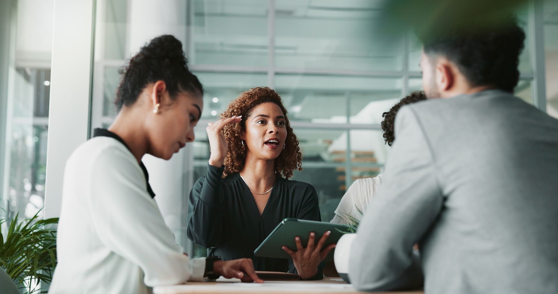 Three people in a meeting, discussing a tablet in a bright office