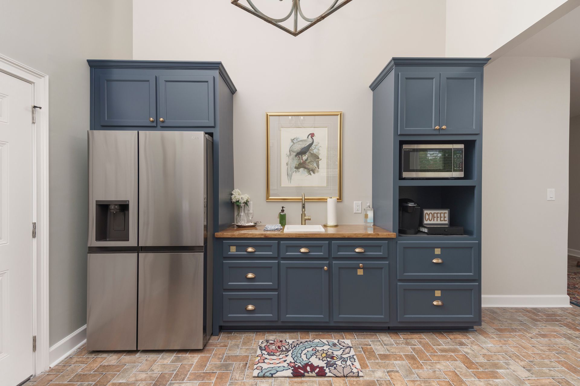 Blue cabinets with a refrigerator, sink, and microwave in a light-filled room.