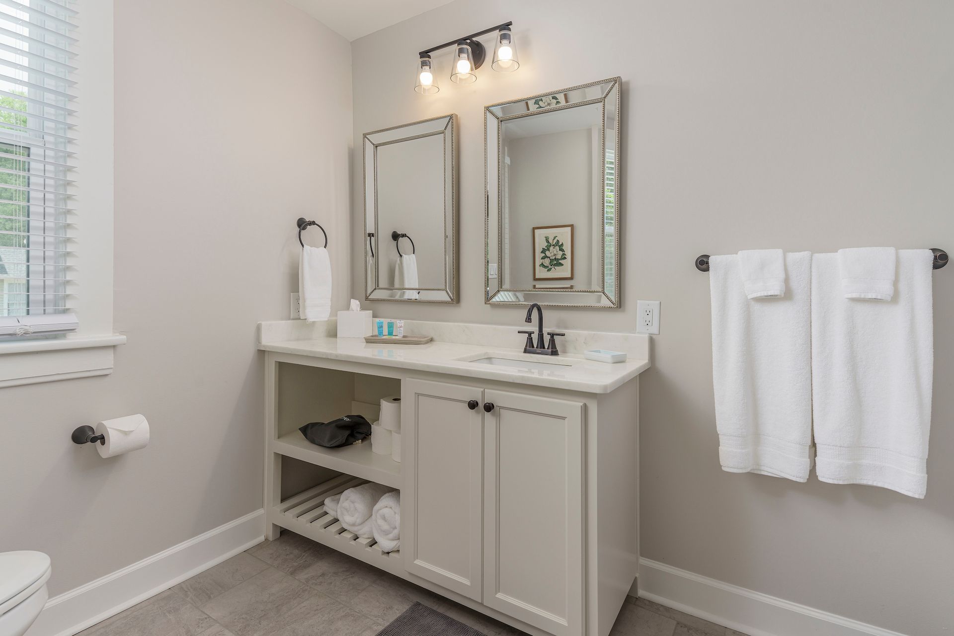 Bathroom with white vanity, two mirrors, and a window. Light gray walls and white towels.