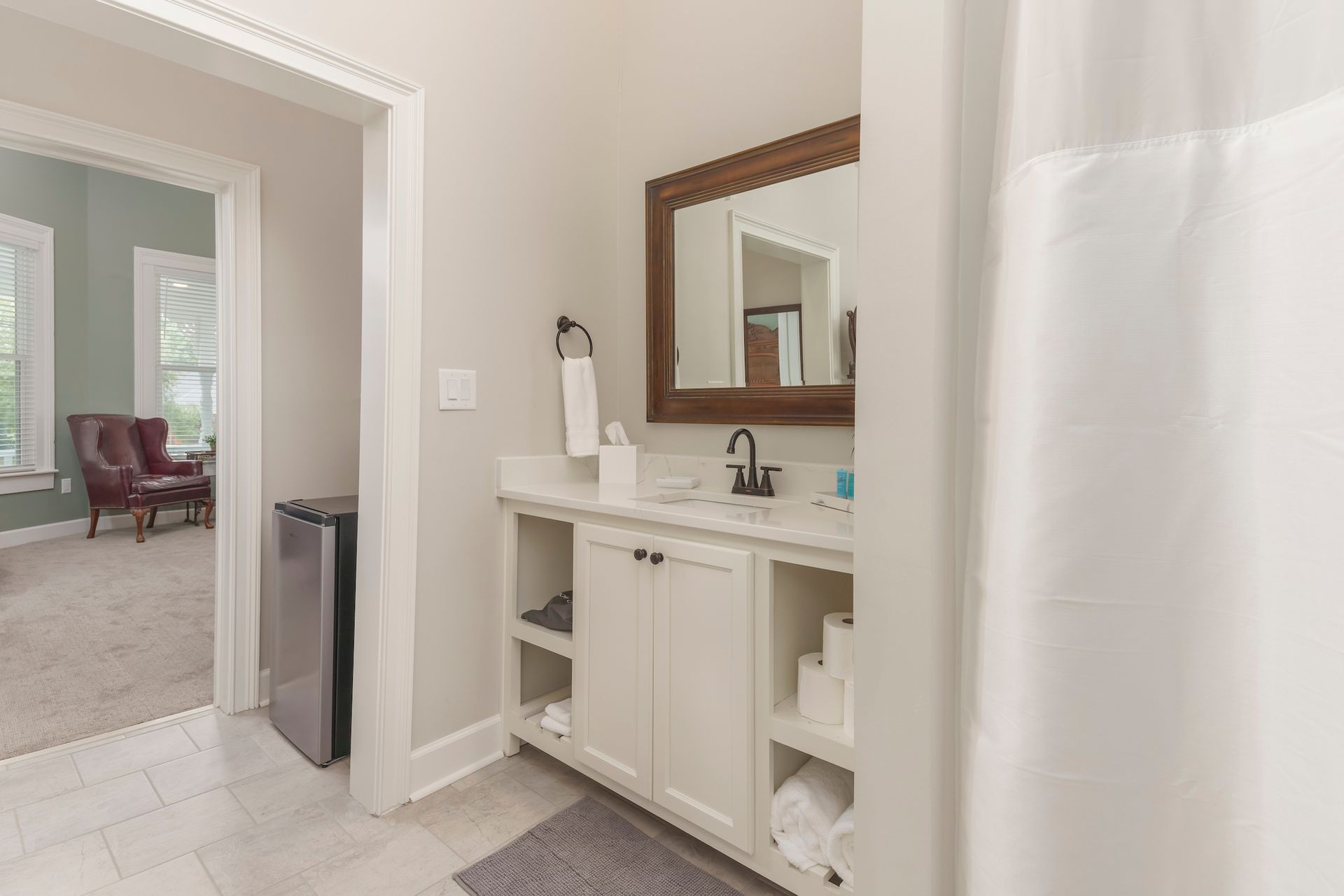 Bathroom with vanity, mirror, and open doorway to a bedroom with seating.