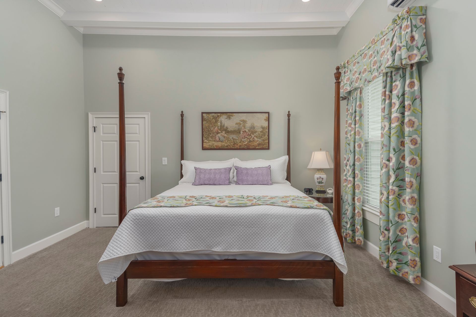 Bedroom with a dark wooden four-poster bed, light blue walls, and patterned curtains.