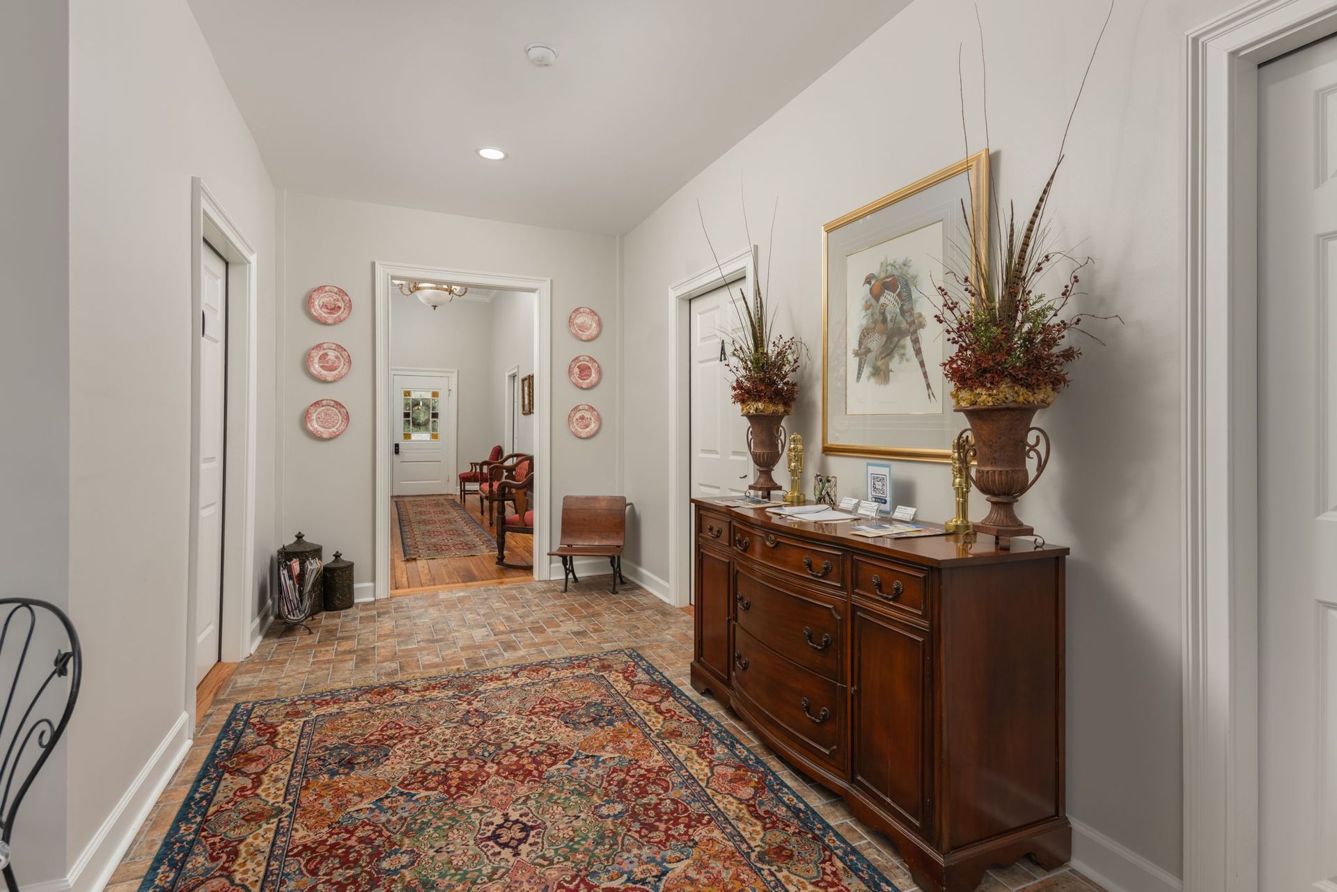 Hallway with a wooden dresser, rug, artwork, and view into another room.