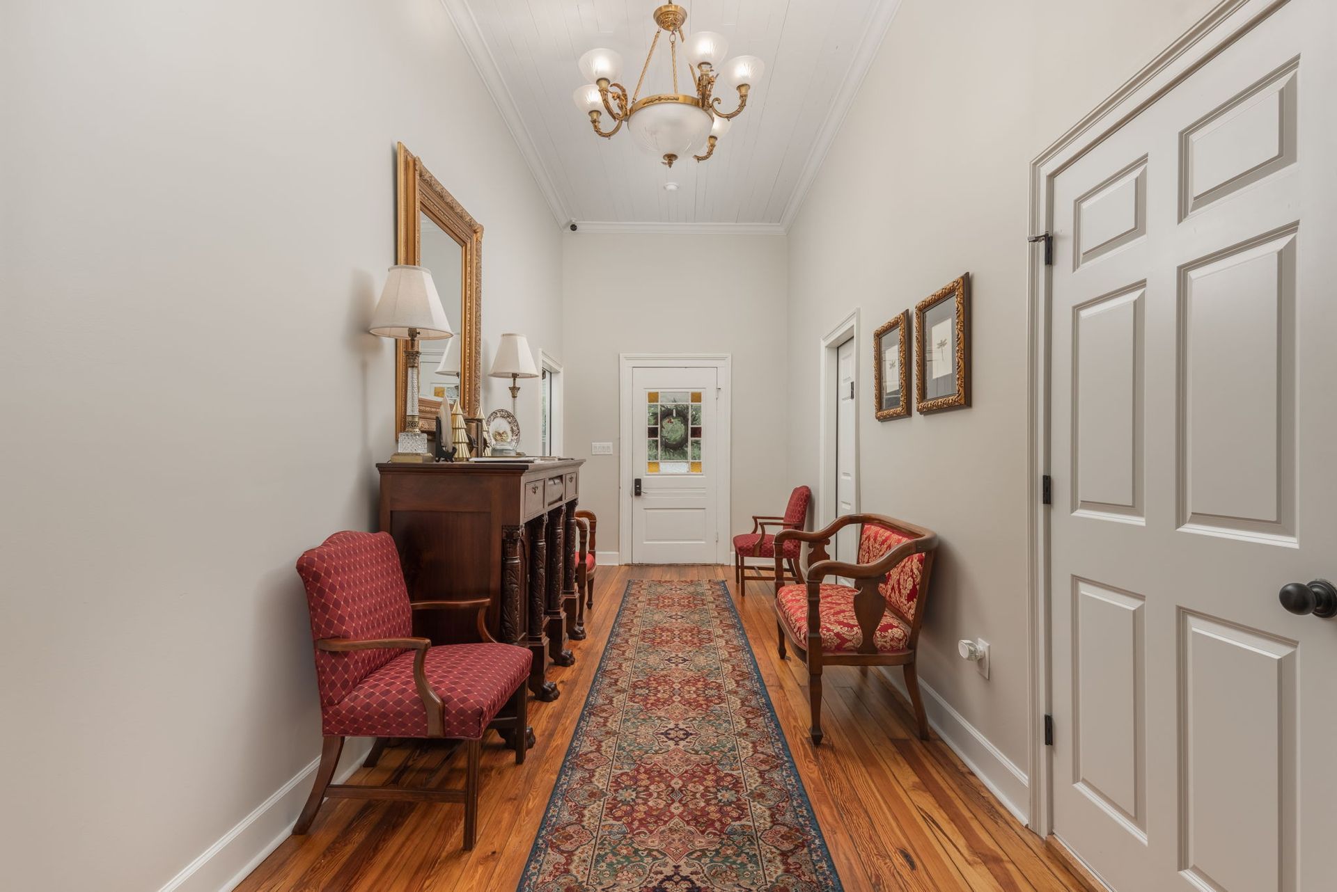 Hallway with wood floors, ornate rug, antique furniture, and white walls.