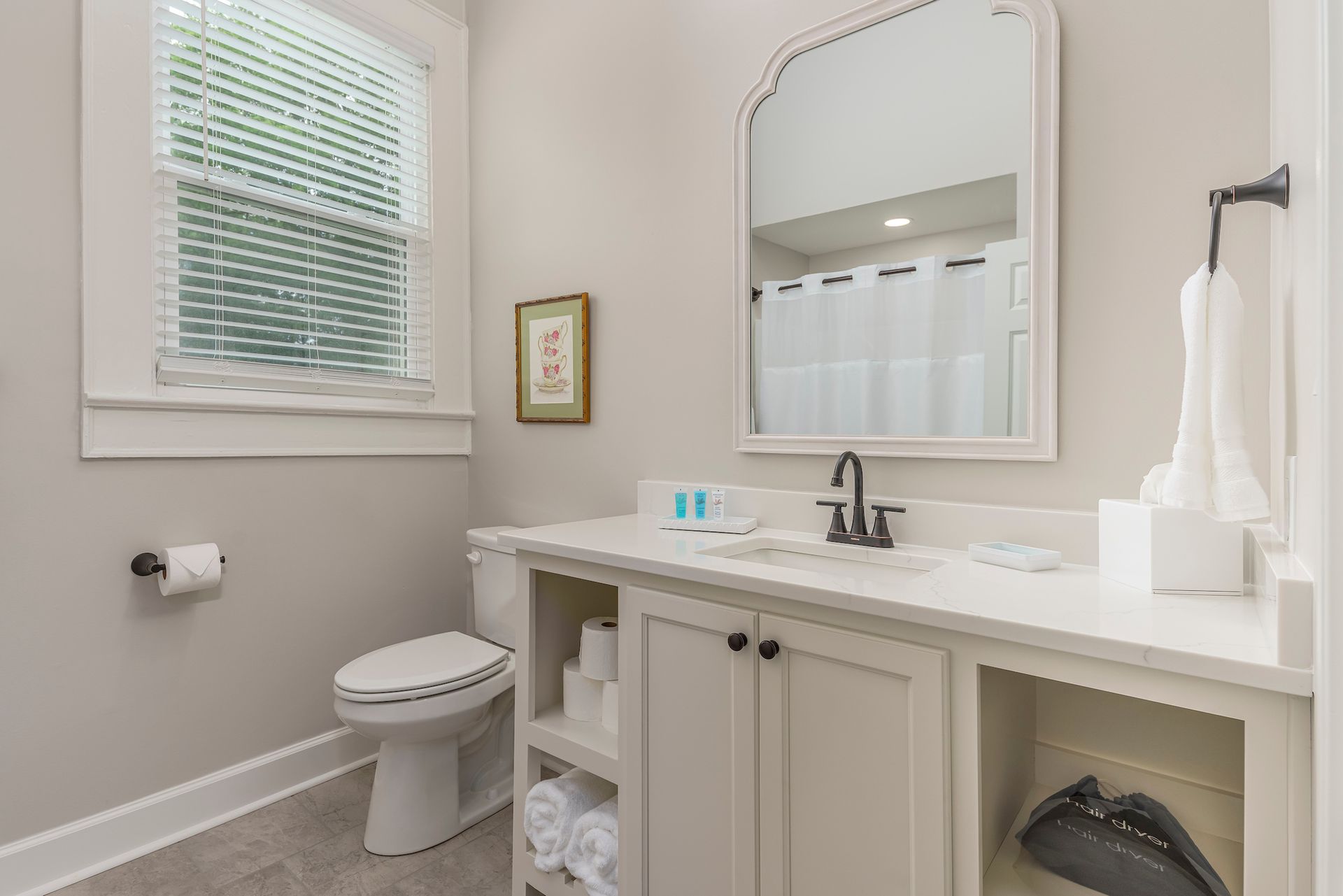 Bathroom with a toilet, vanity, mirror, and window with blinds.