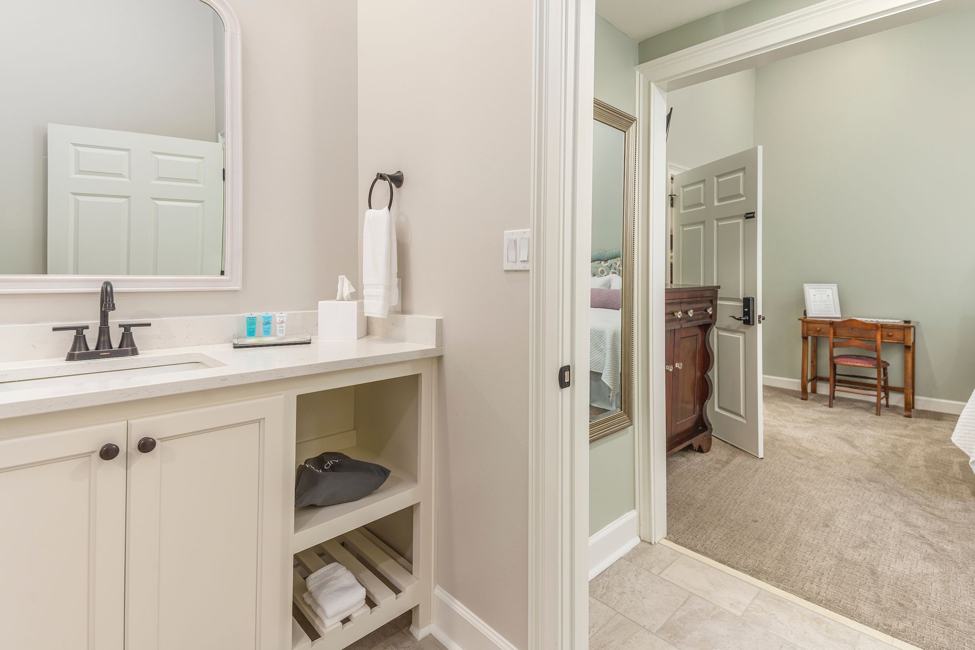 Bathroom with white vanity, open doorway to bedroom, neutral colors.