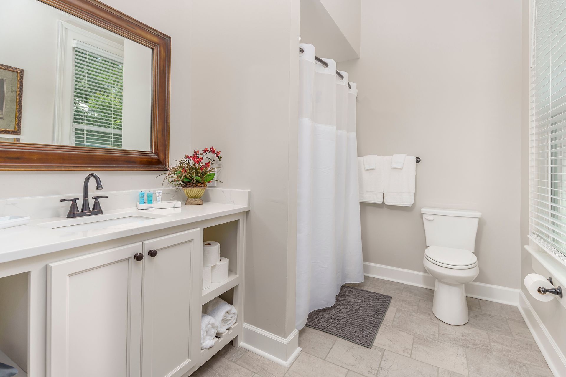 Bathroom with white vanity, toilet, and shower curtain. Gray walls and flooring.