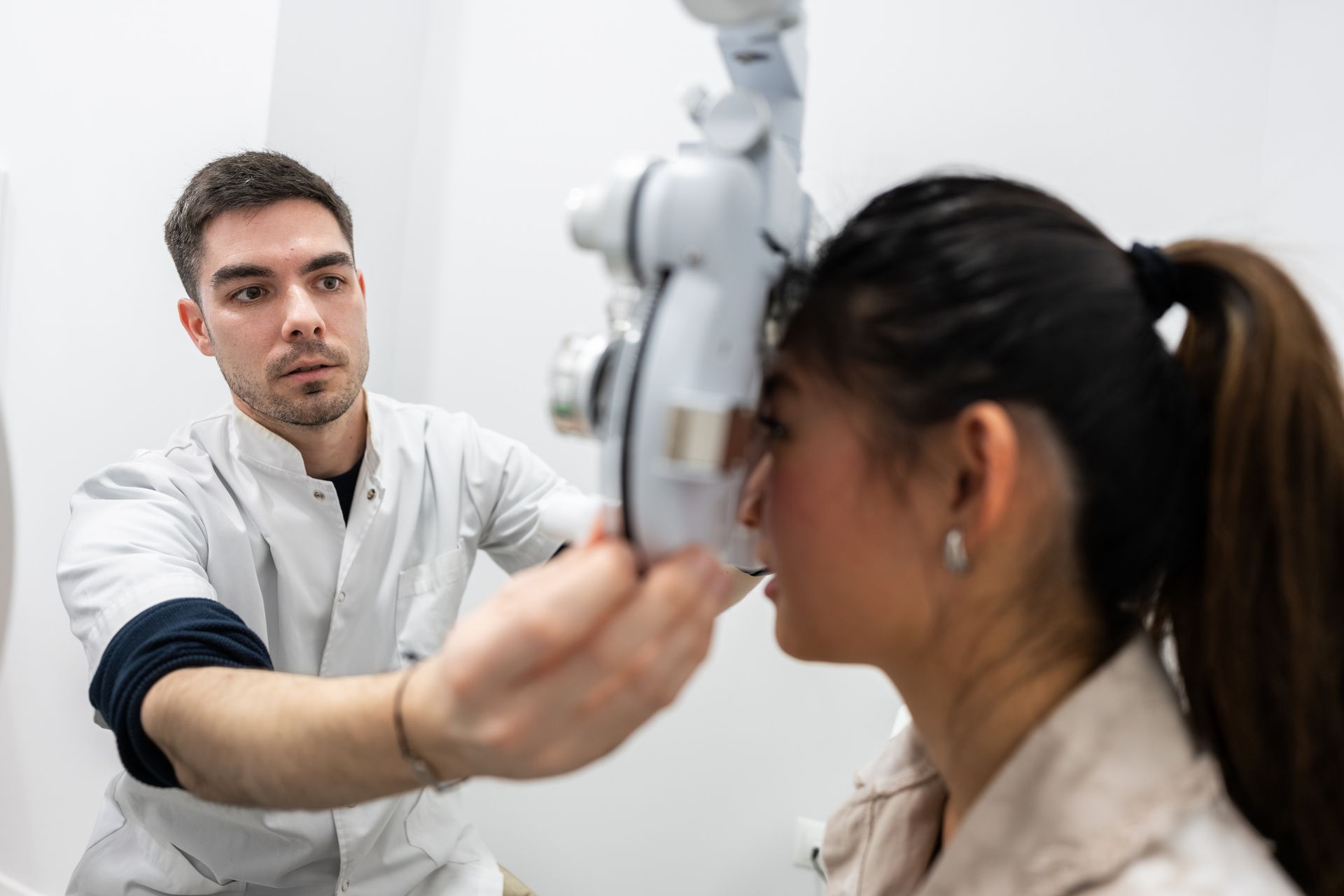 A male eye doctor checks a patient's eye using an examination tool in a medical office.