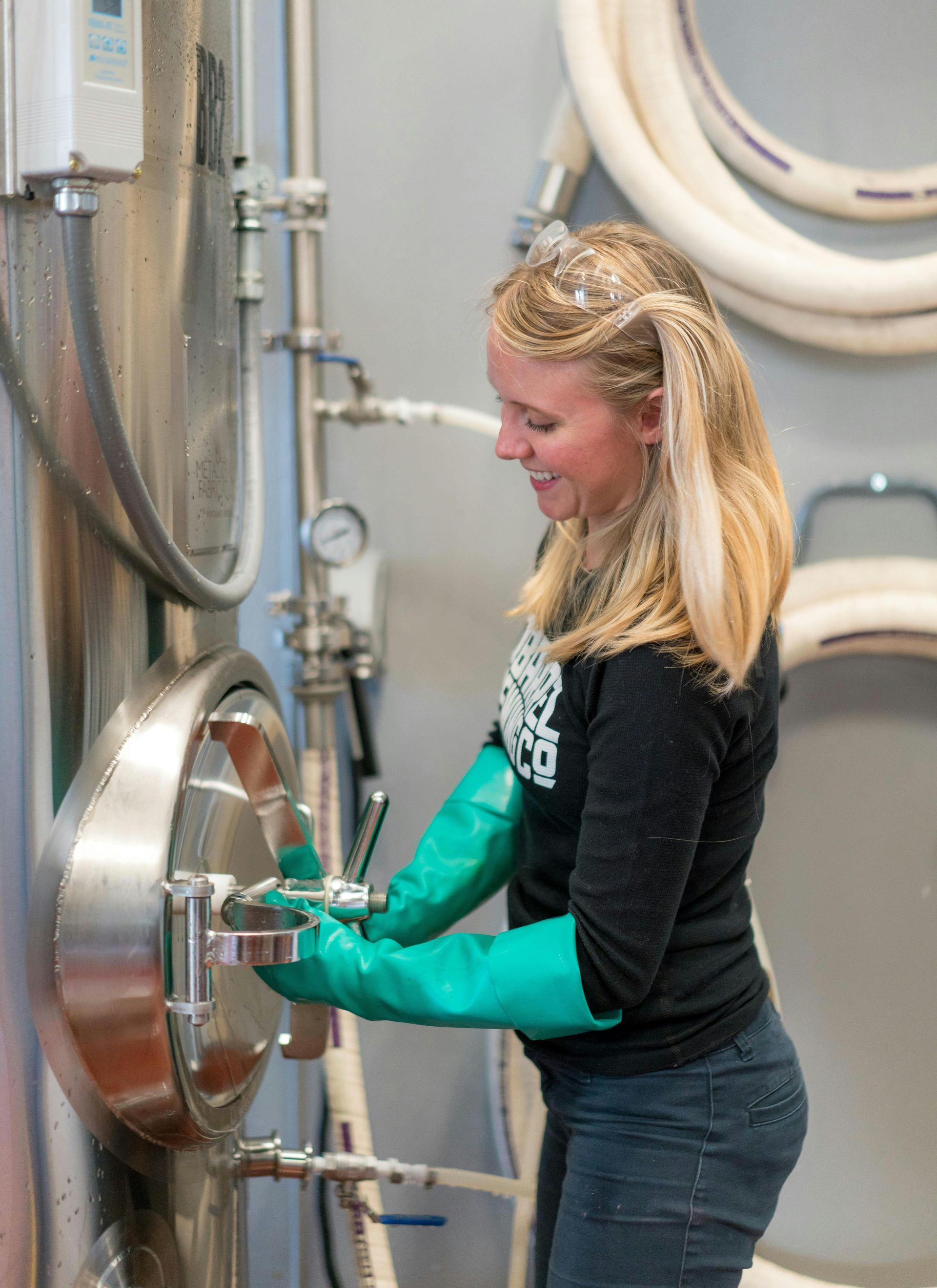 A woman wearing green gloves is working on a machine.