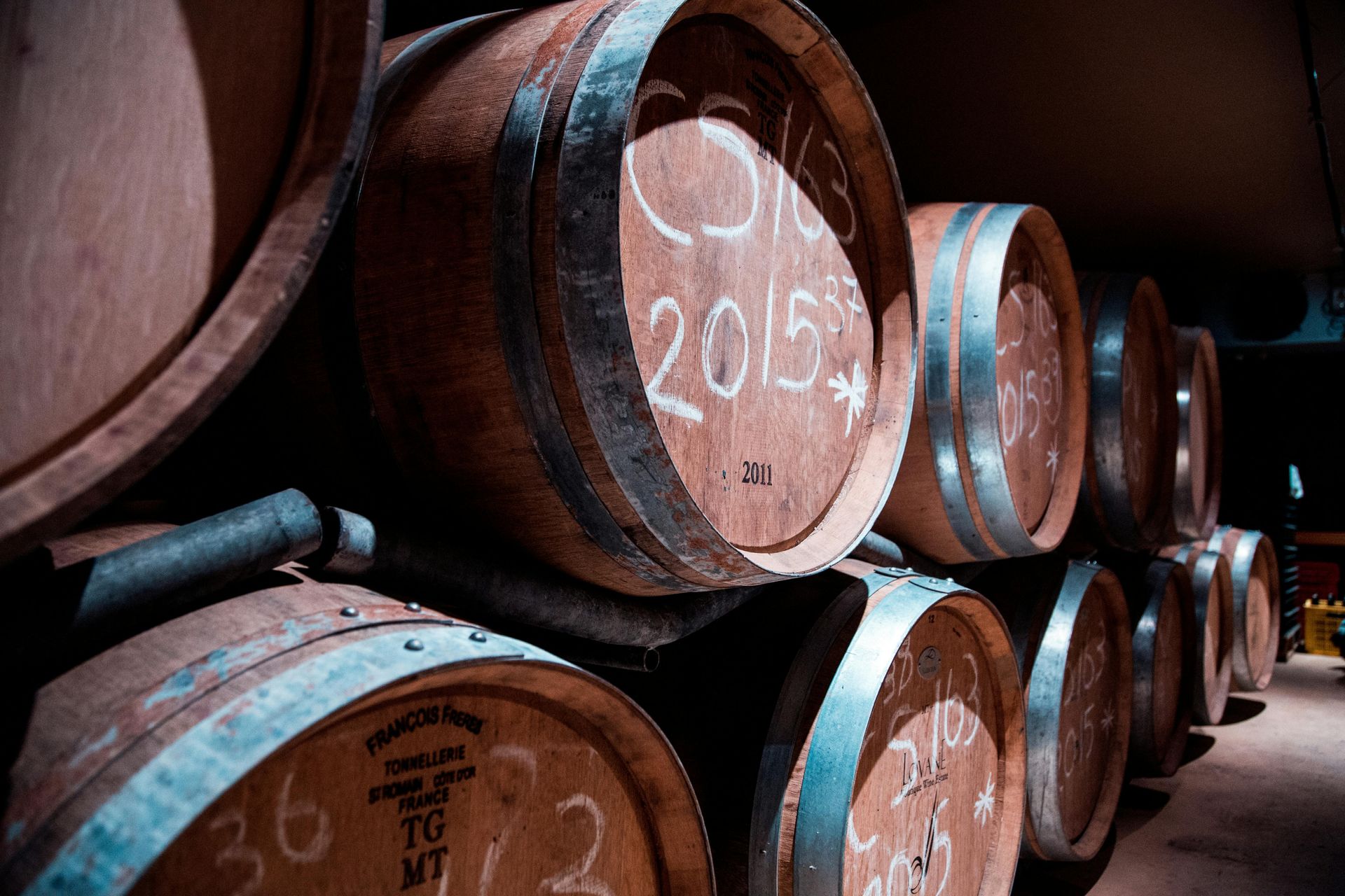 A row of wine barrels are stacked on top of each other in a wine cellar.