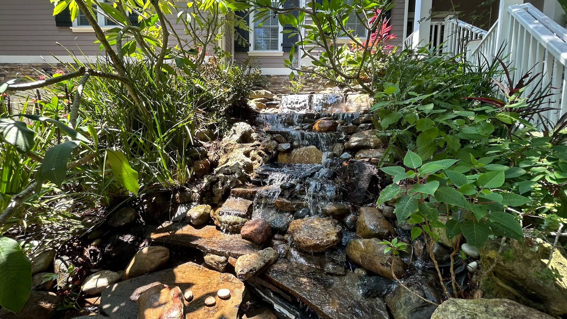 Water cascades down a stone waterfall feature in a garden, framed by lush greenery.