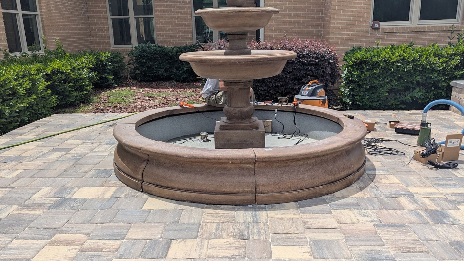 Stone fountain on a brick patio; a person is working on it.
