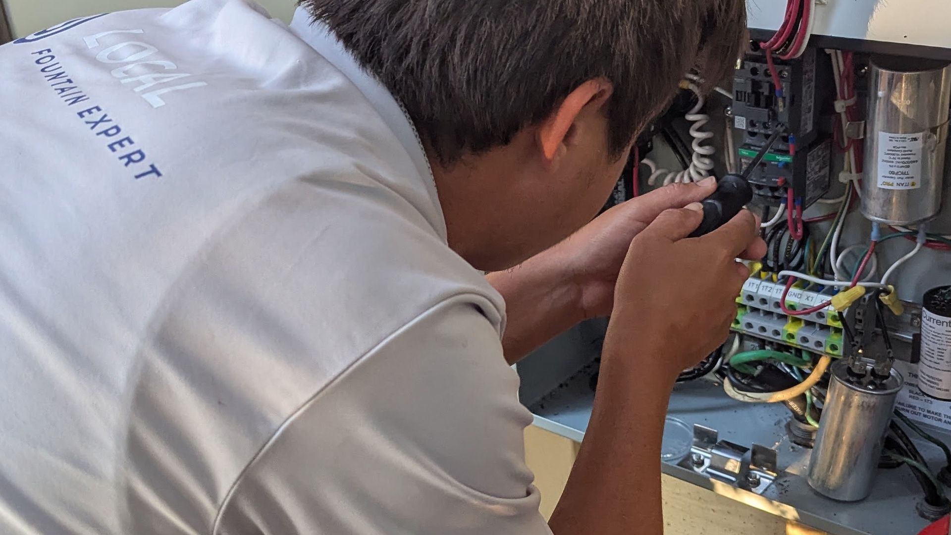 Man working on electrical panel, using a screwdriver; outdoors, sunny.