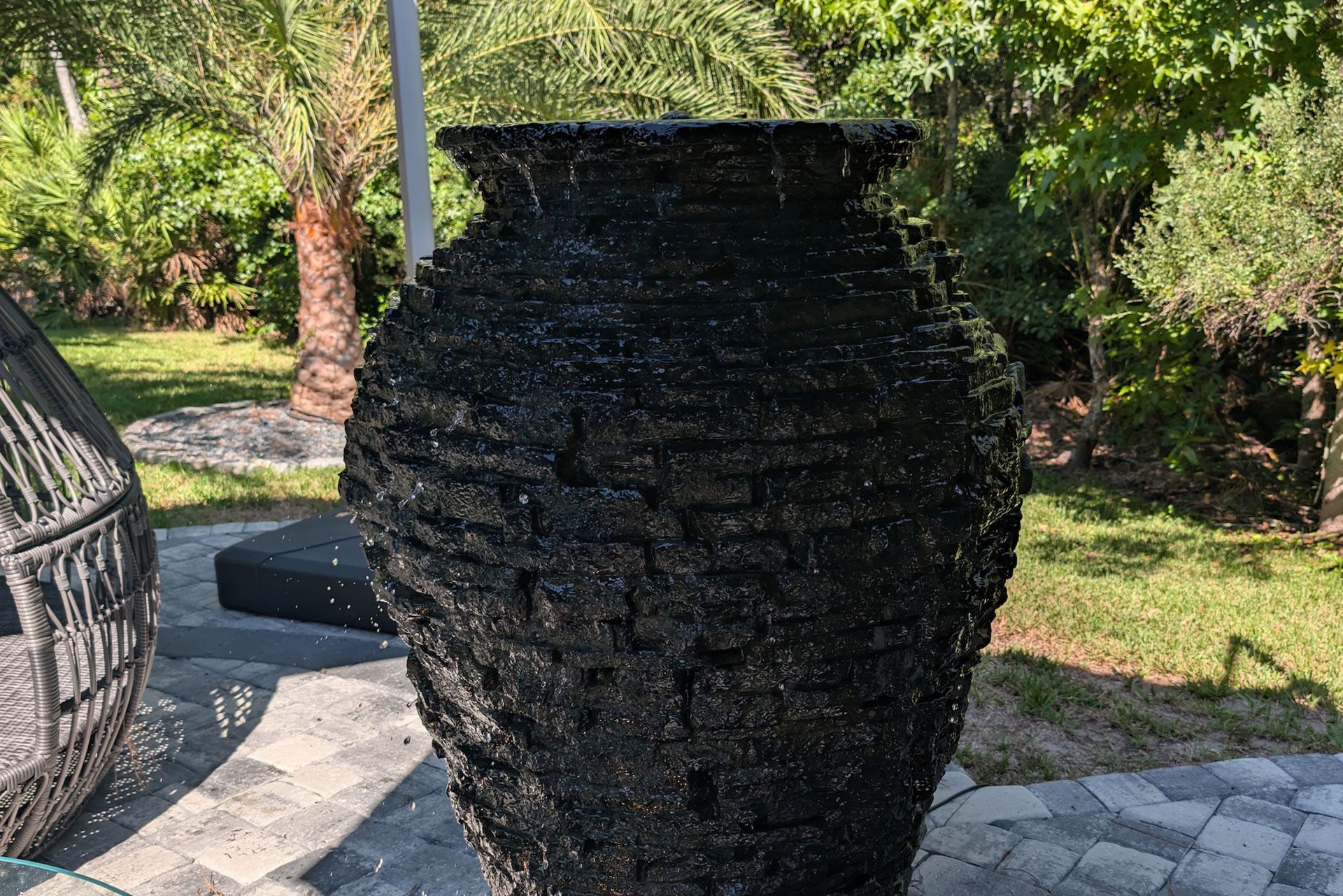 Black textured water fountain in a garden setting.