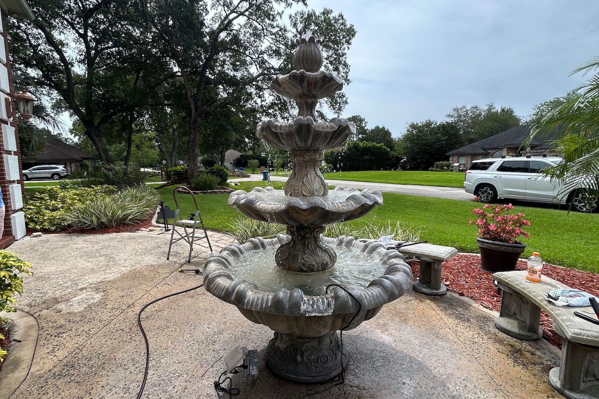 Three-tiered outdoor water fountain with flowing water, set on a patio near a grassy lawn.