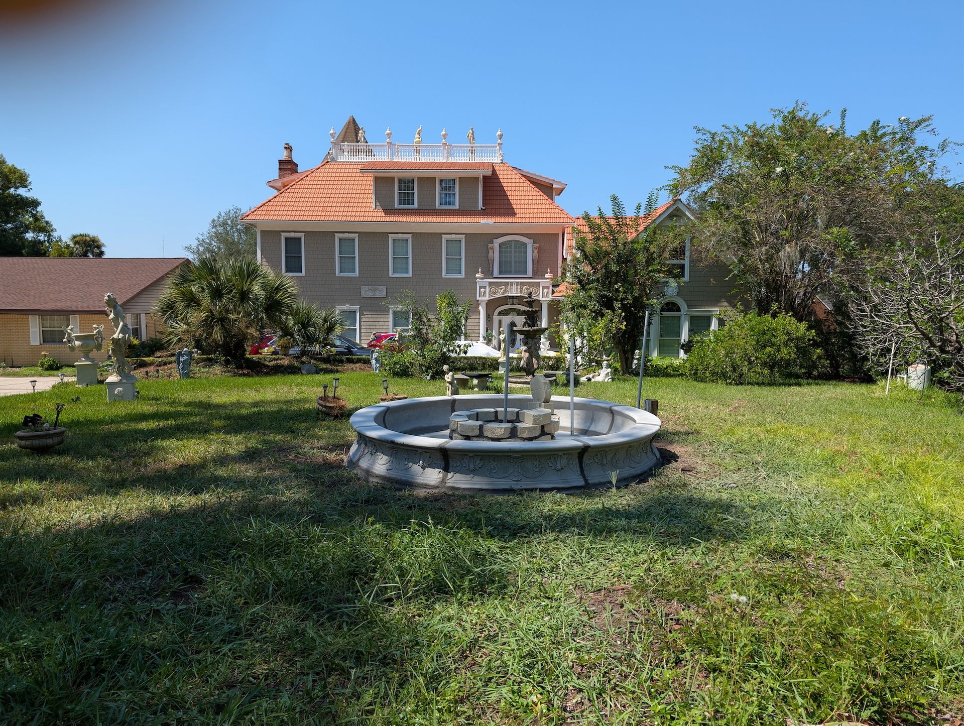 Large stucco house with orange roof, fountain in front lawn, sunny day.