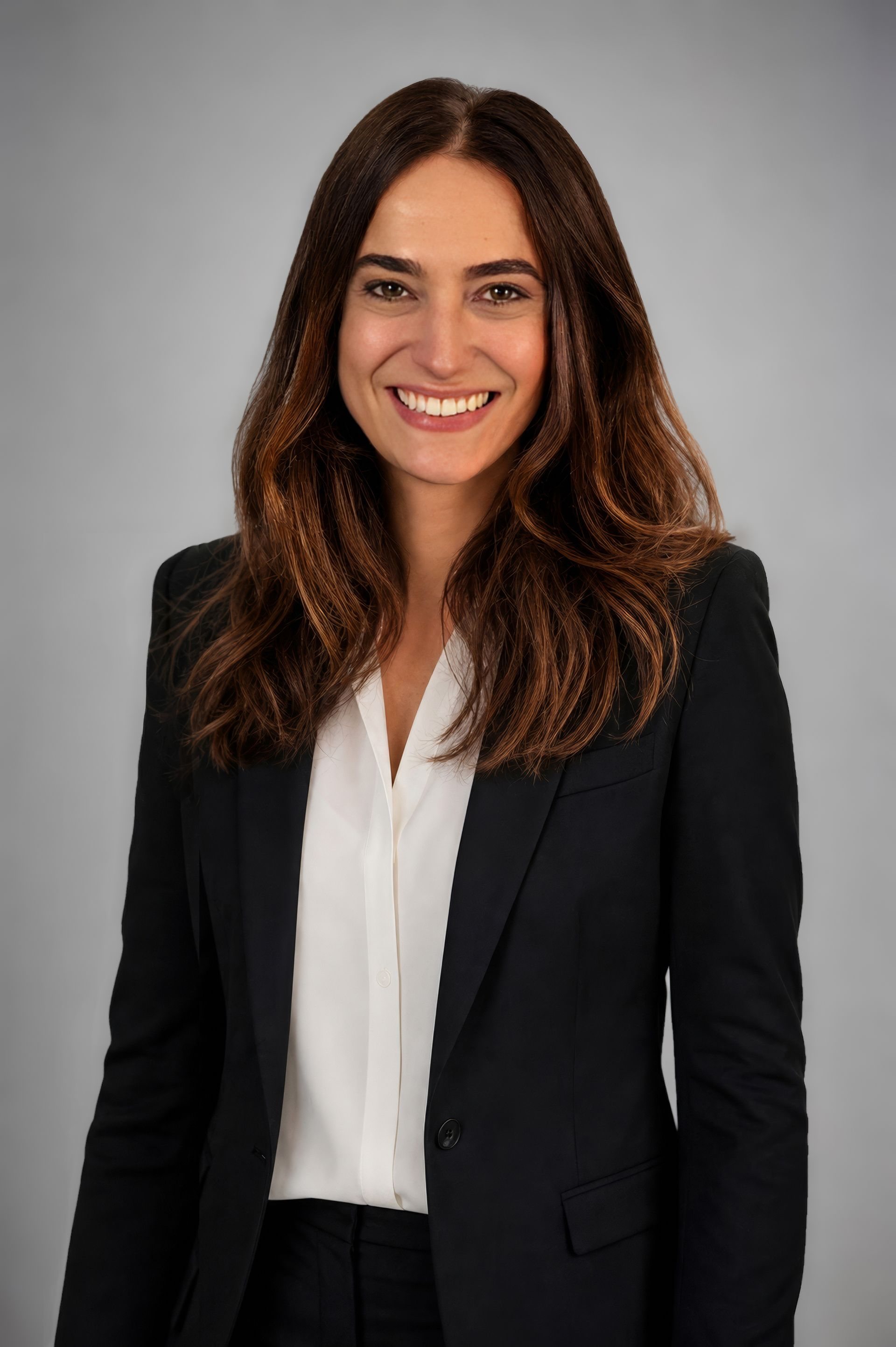 Profesional sonriente con blazer negro y blusa blanca sobre un fondo gris.