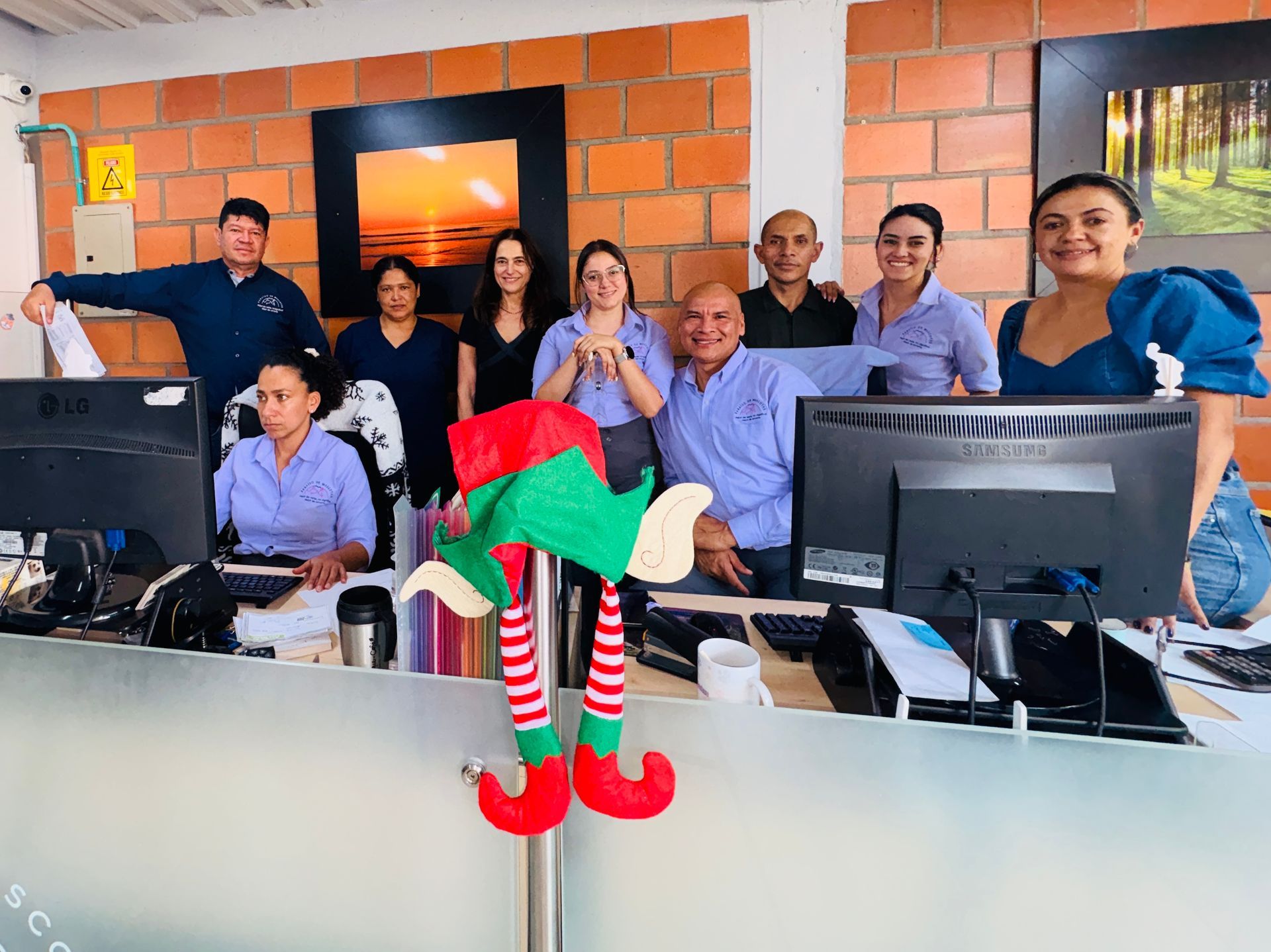 Group of people at computers in an office, with a small red-and-green elf decoration in the foreground