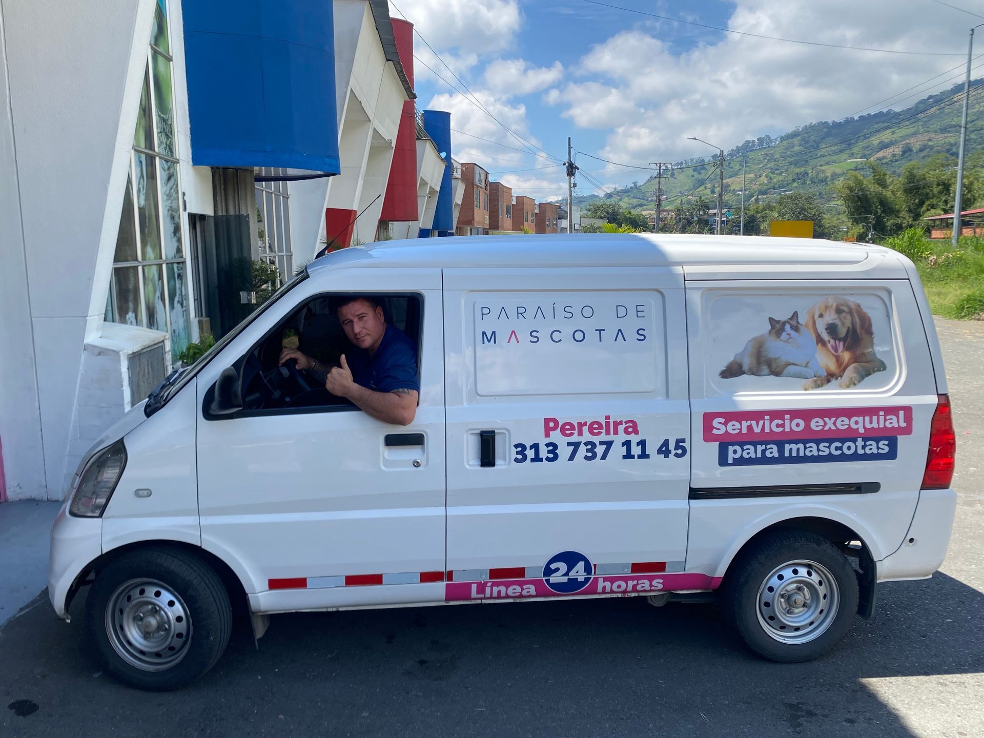 White service van with a driver inside, parked on a street beside buildings and mountains.