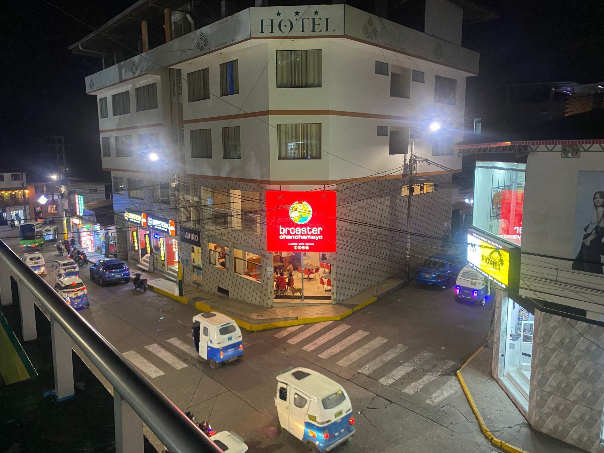 Nighttime street corner with a lit storefront, parked vans, and neon signs on a wet road.