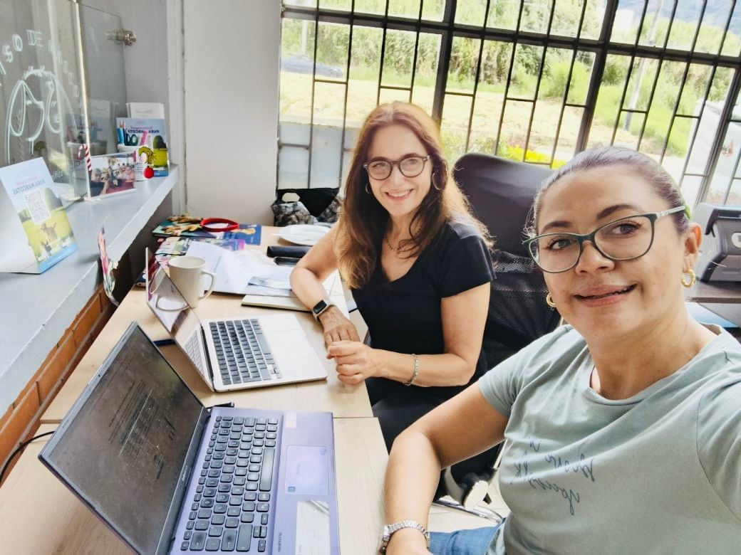 Two people smiling at a desk with laptops in a bright office by a window