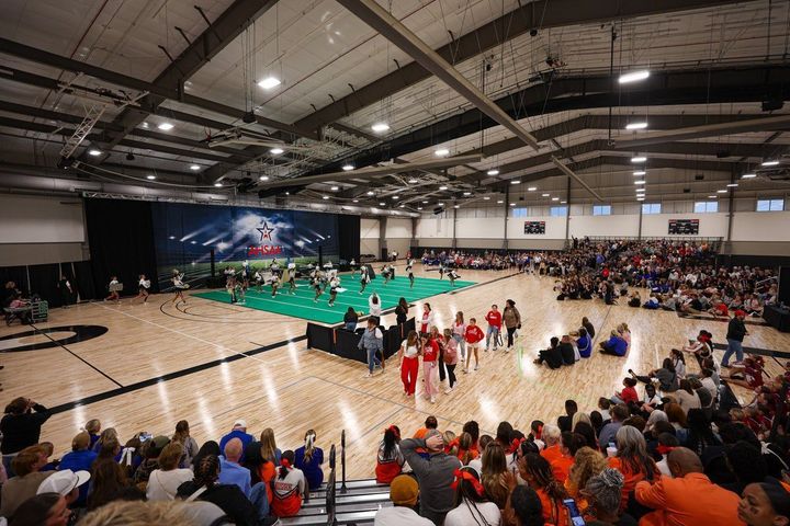 Indoor AHSAA cheerleading in a packed gym, with players on a green court and spectators in the bleachers