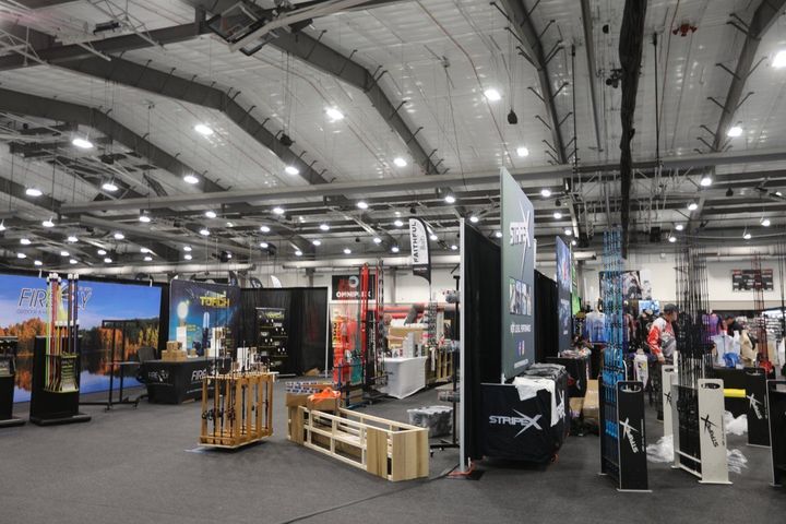 Indoor trade show booth with large banners, displays, and equipment under bright convention hall lights