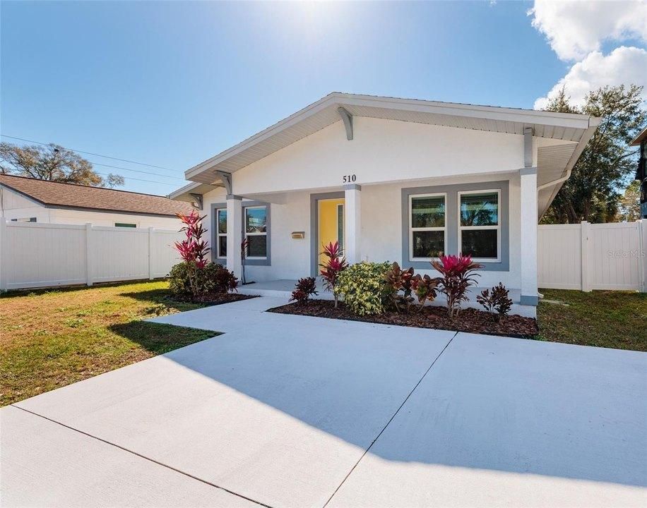 Modern white house with a large driveway, small front porch, and red flowering shrubs.