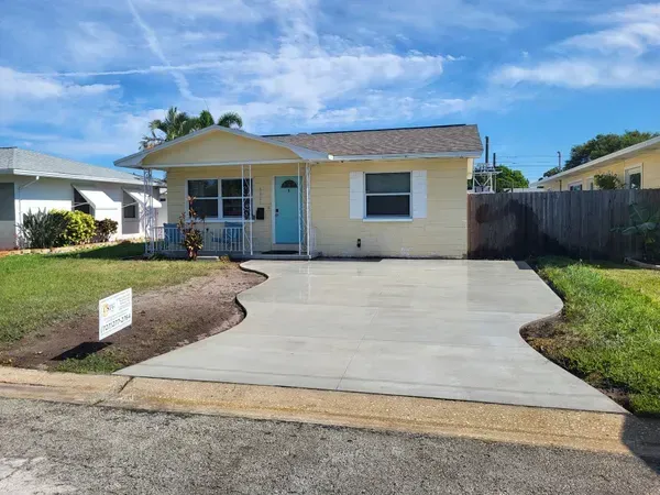 Single-story yellow house with a wide concrete driveway and front lawn under a blue sky