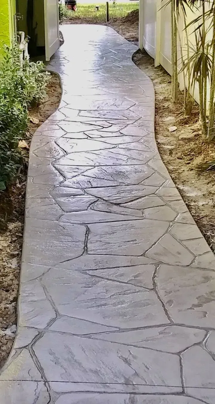 Stone pathway between buildings leading to a gate, with bamboo on the right and plants on the left