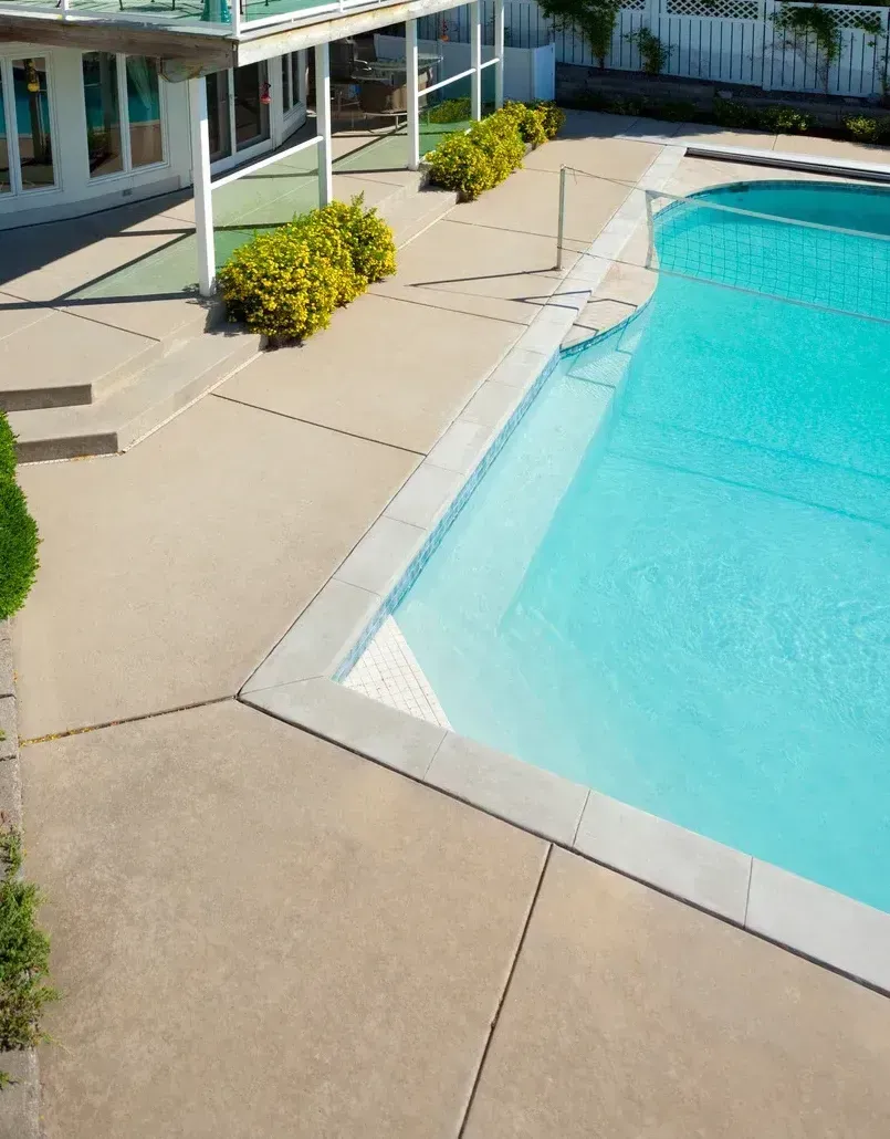 Outdoor swimming pool with turquoise water, beige deck, and white poolside building