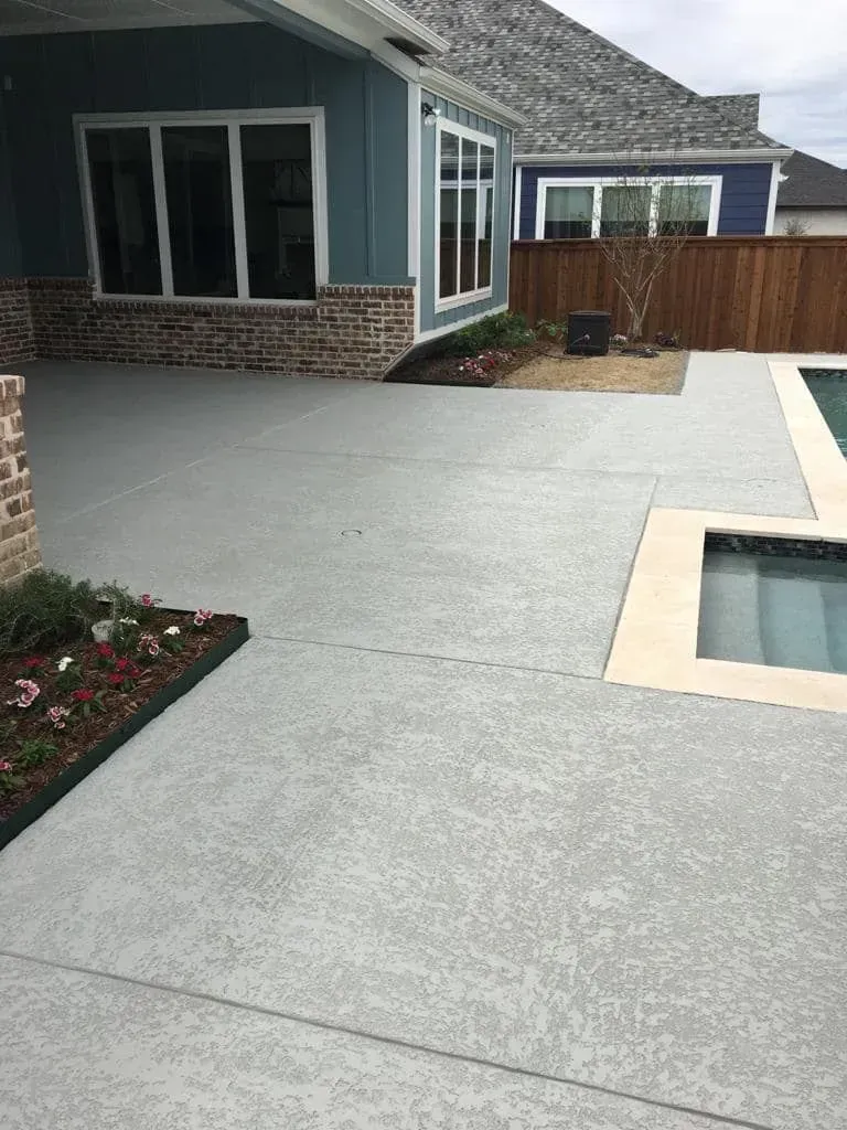 Backyard patio with light gray concrete, brick house, wooden fence, and a small pool or hot tub
