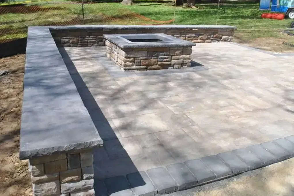 Stone patio with a raised central fire pit and low surrounding wall in a yard