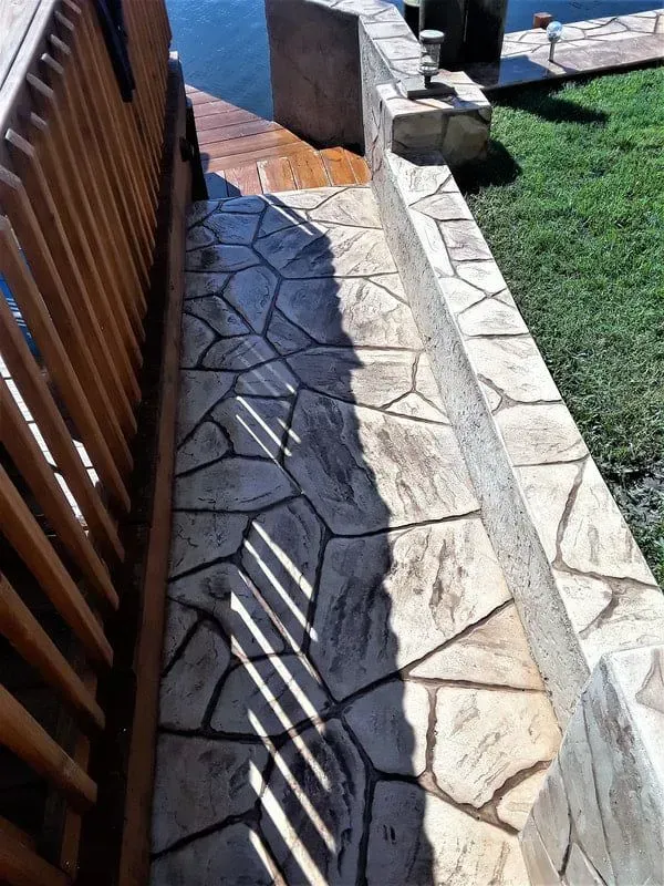 Narrow stone walkway beside a wooden fence, leading toward a gate, with grass on the right.