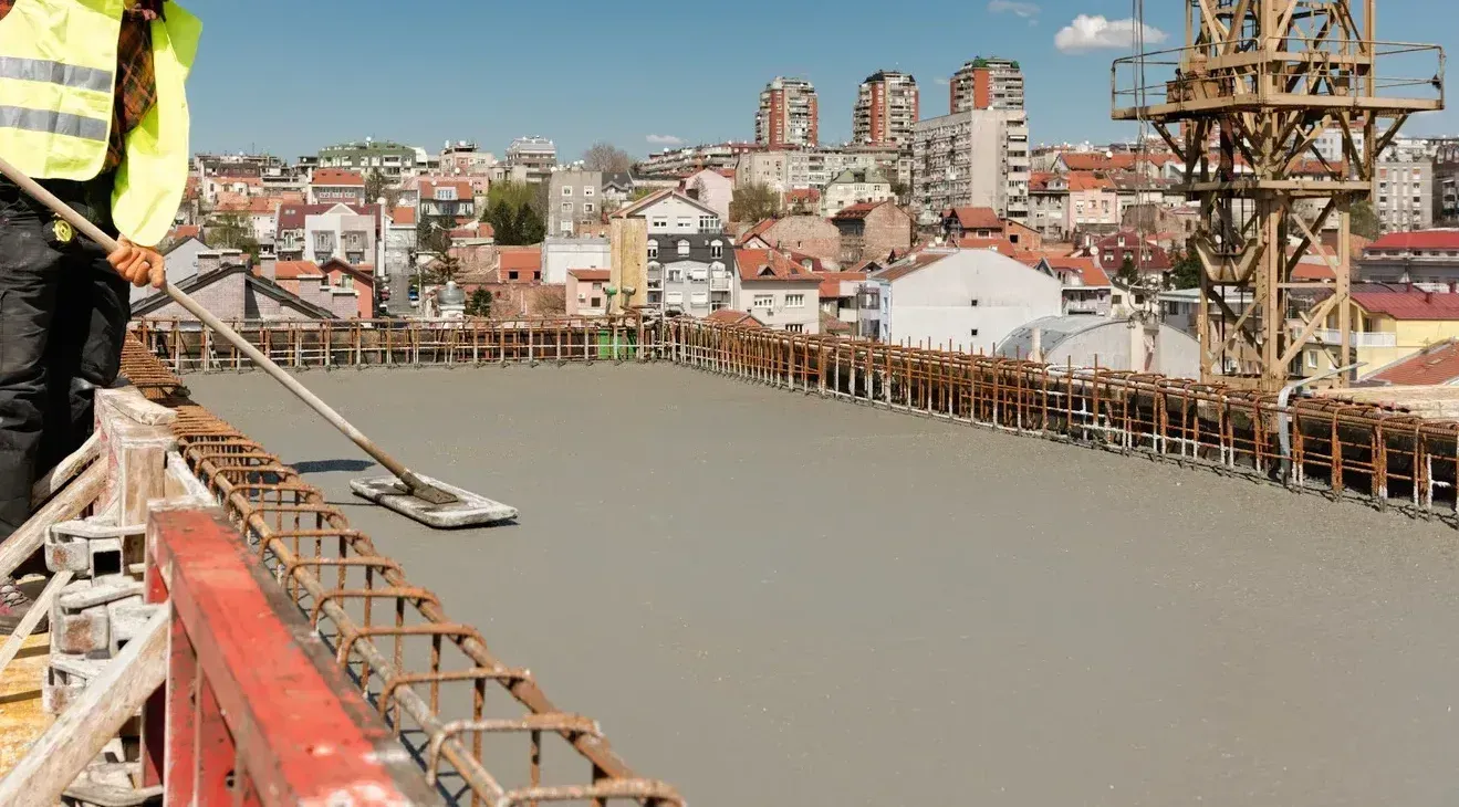Concrete bridge under construction over a river, with a worker in safety gear on the left.