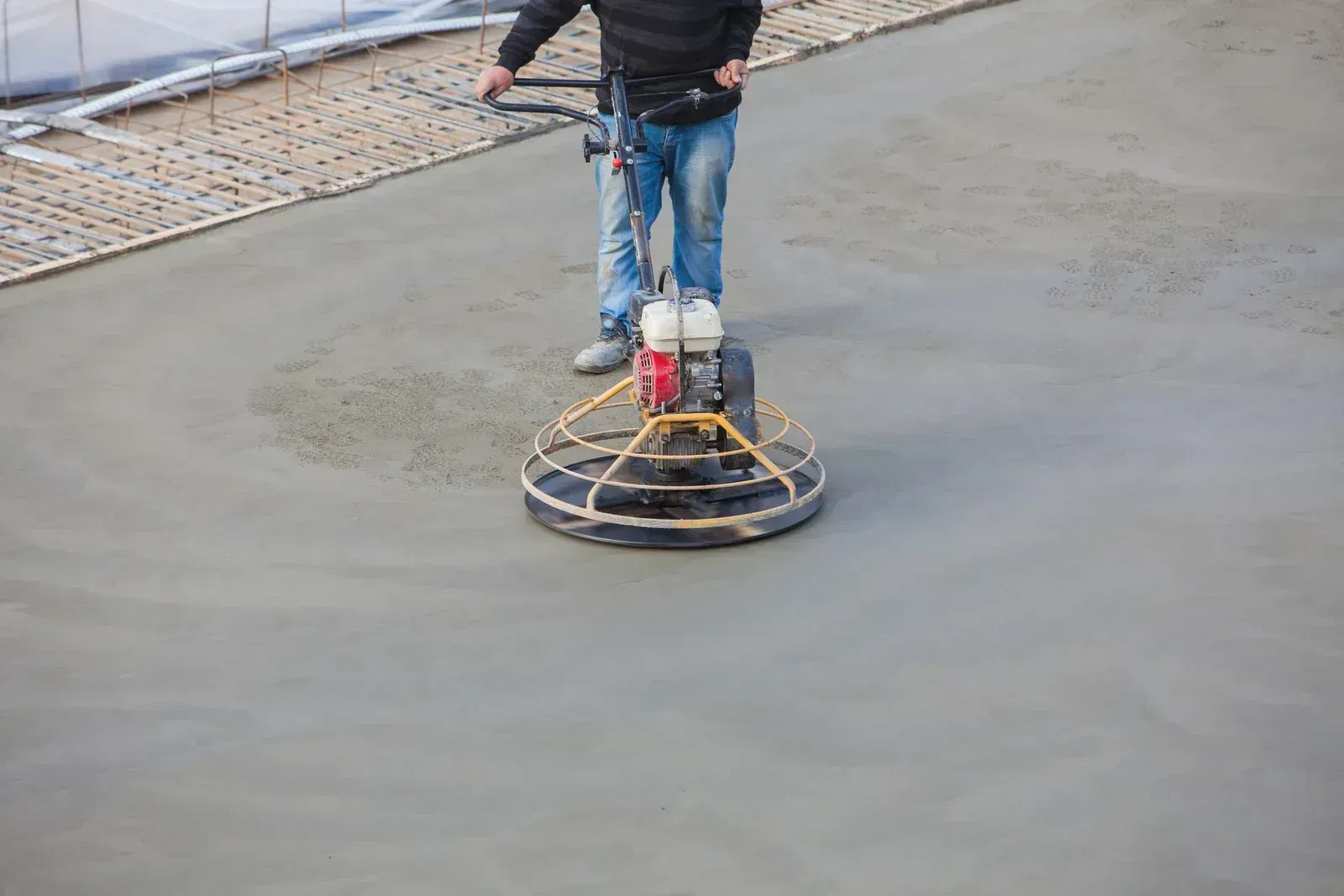 Worker smoothing a concrete floor with a power trowel on a construction site